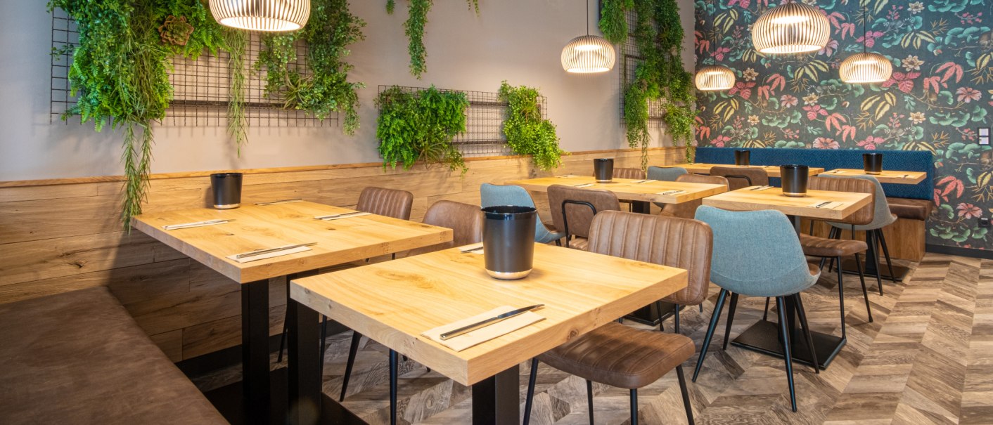 Moderner Frühstücksraum mit Holztischen, bunten Stühlen und Pflanzen an der Wand. Hängelampen und florale Tapete ergänzen das Design., © 13 6 Design GmbH (Judenhof 10, 89073 Ulm) Moderner Frühstücksraum mit Holztischen, bunten Stühlen und Pflanzen an der Wand. Hängelampen und florale Tapete ergänzen das Design., © 13 6 Design GmbH (Judenhof 10, 89073 Ulm)