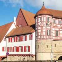 altes Schloss - rechts das Torhaus mit Sockelgeschoss aus hellem Sandstein und aufgesetztem roten Fachwerk mit weißen Gefachen, flankiert von zwei Rundtürmen. In der Bildmitte der Westflügel mit zwei aneinandergebauten, weiß verputzten Gebäudeteilen mit roten Fensterläden, überragt vom Dach und rotbraun gestrichener Giebelseite des Nordflügels. Alle Gebäudeteile eingedekct mit roten Ziegeln. Links das Fachwerkgebäude der ehemaligen Bentheimschen Forstverwaltung mit hellem Sandsteinsockel und grünen Fensterläden., © Stadt Gaildorf