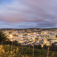 Panorama einer Stadt bei Abenddämmerung, mit beleuchteten Gebäuden und einem bewölkten Himmel im Hintergrund., © SMG, Werner Dieterich