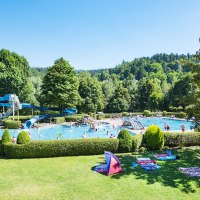Freibad Bad Liebenzell mit blauer Rutsche, Schwimmern im Wasser und gr&uuml;ner Umgebung. Menschen entspannen auf der Wiese unter blauem Himmel., &copy; LOCHER Fotodesing & Manufaktur