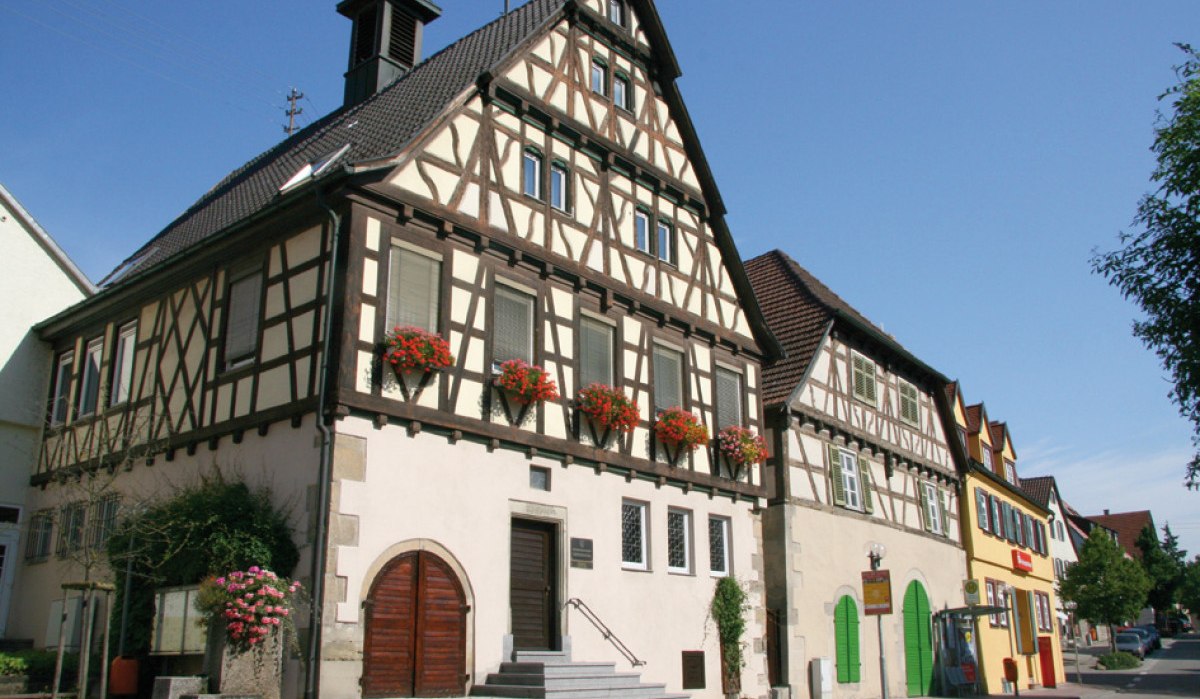Fachwerk-Rathaus in Oberriexingen mit Blumen an den Fenstern, daneben weitere bunte Gebäude. Blauer Himmel im Hintergrund., © Land der 1000 Hügel - Kraichgau-Stromberg