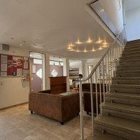 Heller Eingangsbereich mit Treppe, braunen Sofas und Infotafel. Moderne Beleuchtung und Fliesenboden schaffen eine einladende Atmosph&auml;re., &copy; TOMAS