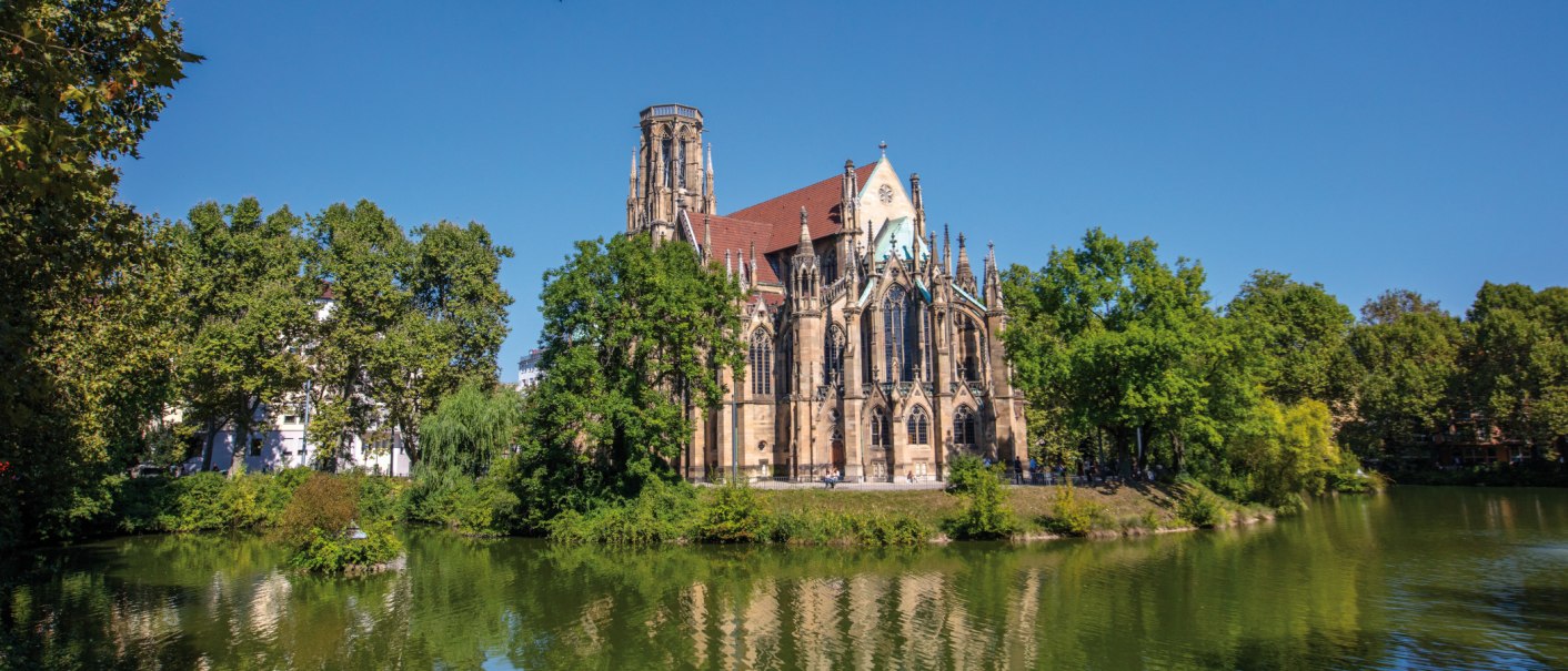 Die Johanneskirche am Feuersee in Stuttgart, umgeben von B&auml;umen und reflektiert im Wasser, bei klarem, sonnigem Wetter., &copy; SMG Achim Mende