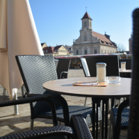 Leerer Außenbereich eines Cafés mit Tischen und Stühlen, im Hintergrund eine Kirche bei klarem Himmel., © Konditorei Lutz