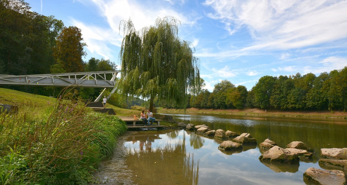 Eine Landungsbr&uuml;cke am Neckarufer mit Menschen, die auf einer Holzplattform sitzen. Ein Baum spendet Schatten, der Himmel ist blau mit wei&szlig;en Wolken., &copy; Fellbach Tourismus