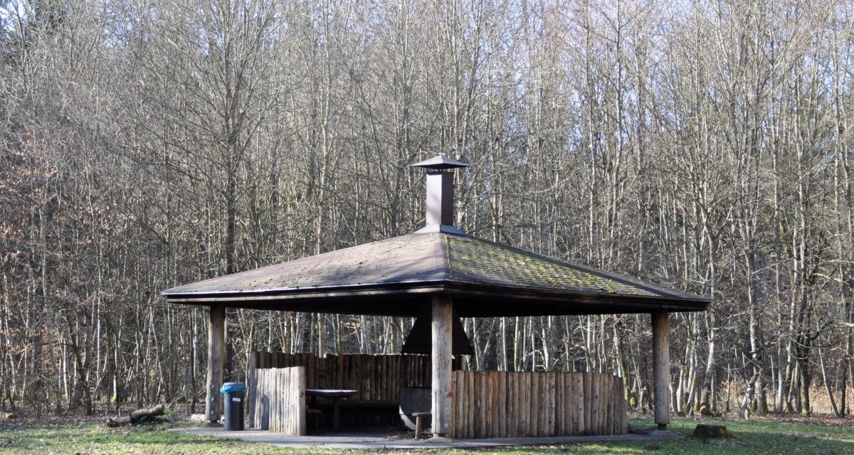 Eine hölzerne Grillhütte mit einem Dach und einem Schornstein steht auf einer Lichtung, umgeben von kahlen Bäumen., © Natur.Nah. Schönbuch & Heckengäu Eine hölzerne Grillhütte mit einem Dach und einem Schornstein steht auf einer Lichtung, umgeben von kahlen Bäumen., © Natur.Nah. Schönbuch & Heckengäu