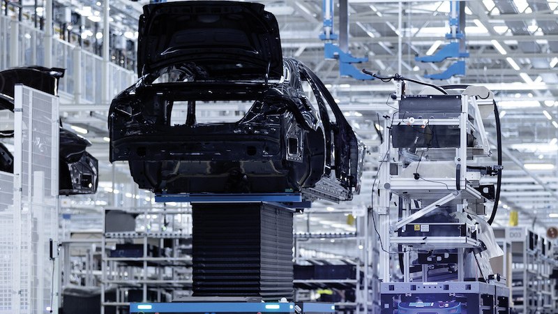 Eine moderne Fabrikhalle zeigt die Fahrzeugmontage mit Robotern und Fahrzeugkarosserien. Die Umgebung ist hell und technologisch fortschrittlich., &copy; Mercedes-Benz AG