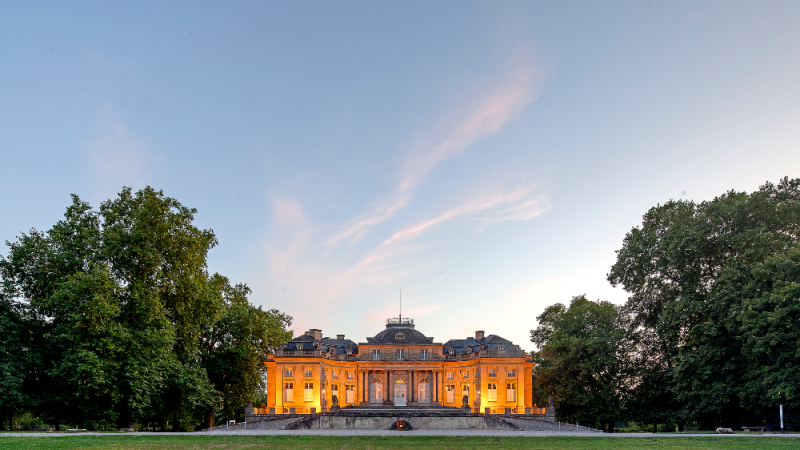 Das Seeschloss Monrepos leuchtet in warmem Licht bei Sonnenuntergang, umgeben von &uuml;ppigen B&auml;umen und einem weiten Rasen., &copy; Seeschloss Monrepos &copy; Daniel Stauch
