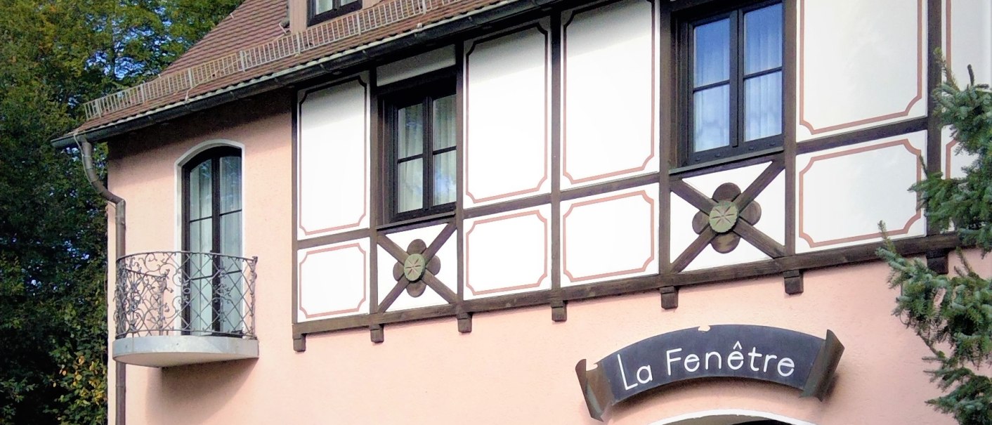 Fachwerkhaus mit Schild 'La Fenêtre', kleinem Balkon, gepflegtem Garten und blühenden Pflanzen vor der Tür., © relexa Waldhotel Schatten Fachwerkhaus mit Schild 'La Fenêtre', kleinem Balkon, gepflegtem Garten und blühenden Pflanzen vor der Tür., © relexa Waldhotel Schatten
