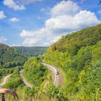 Ein Wanderer blickt vom Mühltalfelsen auf die kurvenreiche Geislinger Steige, wo ein Zug durch die grüne Landschaft fährt., © Landkreis Göppingen Ein Wanderer blickt vom Mühltalfelsen auf die kurvenreiche Geislinger Steige, wo ein Zug durch die grüne Landschaft fährt., © Landkreis Göppingen