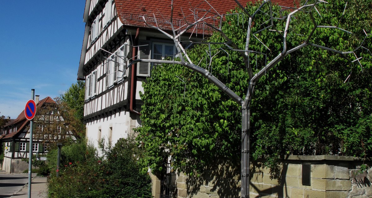 Brunnen mit Metallstruktur vor Fachwerkhaus und blauem Himmel. Historische Architektur und grüne Vegetation im Hintergrund., © RadL Leonberg Brunnen mit Metallstruktur vor Fachwerkhaus und blauem Himmel. Historische Architektur und grüne Vegetation im Hintergrund., © RadL Leonberg