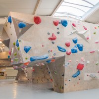 Innenansicht der VELS Boulderhalle mit Kletterwänden und bunten Griffen unter einem gewölbten Dach., © Boulderhalle Vels