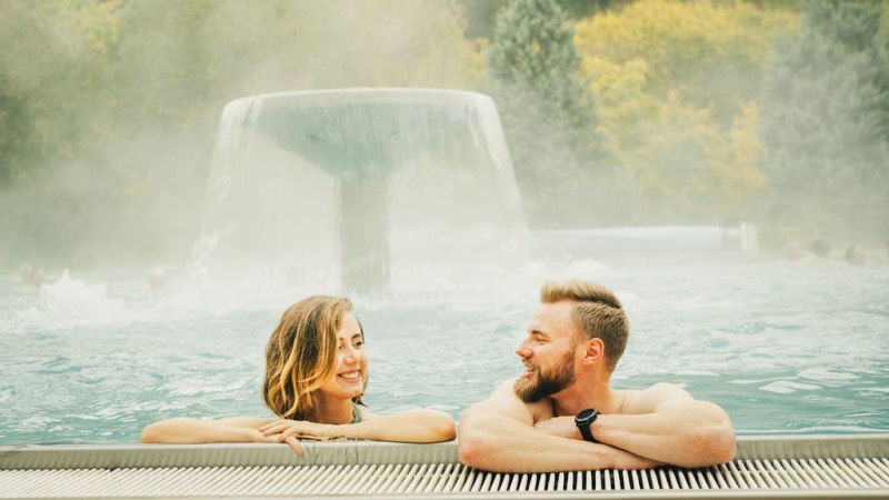 Zwei Personen entspannen in einem Außenpool der Paracelsus-Therme Bad Liebenzell. Im Hintergrund ein Wasserfall und bewaldete Hügel., © LOCHER Fotodesign & Manufaktur