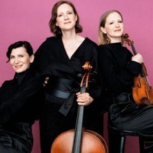 Das Boulanger Trio posiert mit Cello und Violine vor einem rosa Hintergrund. Die Musikerinnen tragen schwarze Kleidung., © links im Bild Das Boulanger Trio posiert mit Cello und Violine vor einem rosa Hintergrund. Die Musikerinnen tragen schwarze Kleidung., © links im Bild