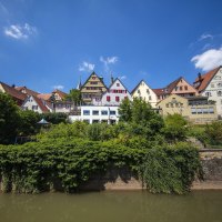 Bunte Fachwerkhäuser auf einem Hügel über einem Fluss, umgeben von Bäumen, unter blauem Himmel., © Stuttgart Marketing GmbH Achim Mende