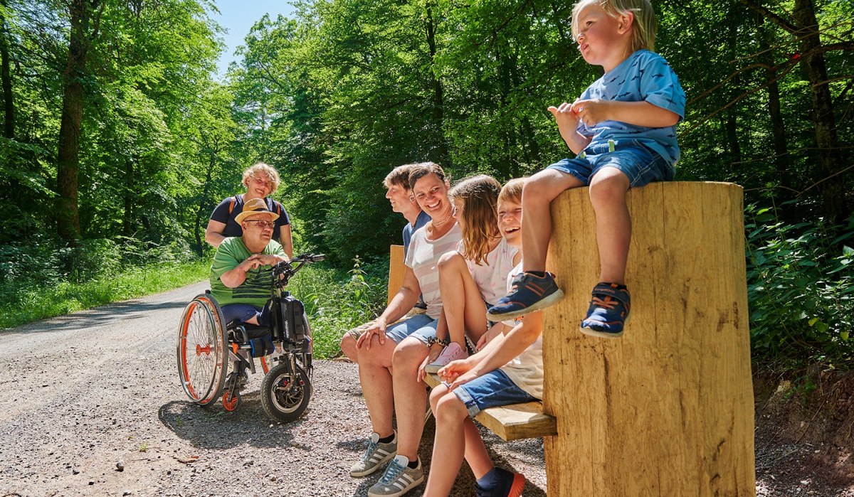 Menschen sitzen und stehen auf einem Waldweg, darunter ein Mann im Rollstuhl. Sie lachen und genießen die Natur., © Natur.Nah. Schönbuch & Heckengäu Menschen sitzen und stehen auf einem Waldweg, darunter ein Mann im Rollstuhl. Sie lachen und genießen die Natur., © Natur.Nah. Schönbuch & Heckengäu