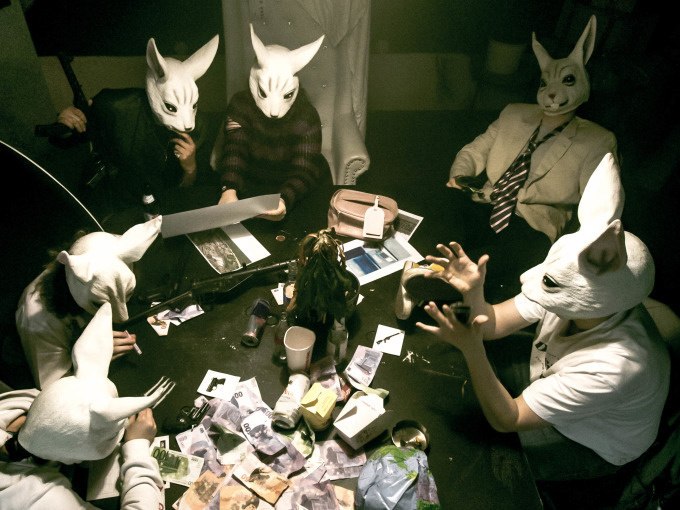 Personen mit Hasenmasken sitzen an einem Tisch voller Geldscheine und Dokumente in einem dunklen Raum., © ExitGames Stuttgart Personen mit Hasenmasken sitzen an einem Tisch voller Geldscheine und Dokumente in einem dunklen Raum., © ExitGames Stuttgart