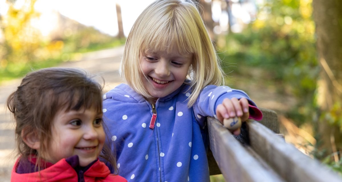 Zwei lachende Kinder spielen an einer Holzkugelbahn im Wald. Eines der Kinder hält eine Kugel in der Hand., © Thomas Zehnder Zwei lachende Kinder spielen an einer Holzkugelbahn im Wald. Eines der Kinder hält eine Kugel in der Hand., © Thomas Zehnder