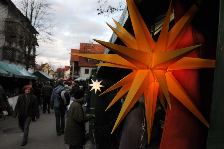 Ein Weihnachtsmarkt mit leuchtendem gelben Stern im Vordergrund. Menschen schlendern durch eine Gasse mit Ständen und Dekorationen., © Gemeinde Bad Boll