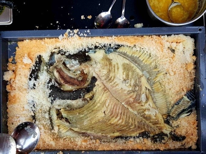Gebackener Fisch in Salzkruste auf einem Blech, umgeben von Löffeln und einer Schüssel mit Soße. Der Fisch ist teilweise freigelegt., © Kultweine-Kochwelten-Kunstücke - Kochschule Sonja Lenz Gebackener Fisch in Salzkruste auf einem Blech, umgeben von Löffeln und einer Schüssel mit Soße. Der Fisch ist teilweise freigelegt., © Kultweine-Kochwelten-Kunstücke - Kochschule Sonja Lenz