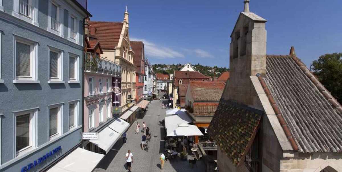 Historische Straßenszene mit alten Gebäuden, Menschen spazieren auf Kopfsteinpflaster. Rechts eine Kirche mit Kreuz, links bunte Fassaden und Geschäfte., © Esslinger Stadtmarketing & Tourismus GmbH Historische Straßenszene mit alten Gebäuden, Menschen spazieren auf Kopfsteinpflaster. Rechts eine Kirche mit Kreuz, links bunte Fassaden und Geschäfte., © Esslinger Stadtmarketing & Tourismus GmbH