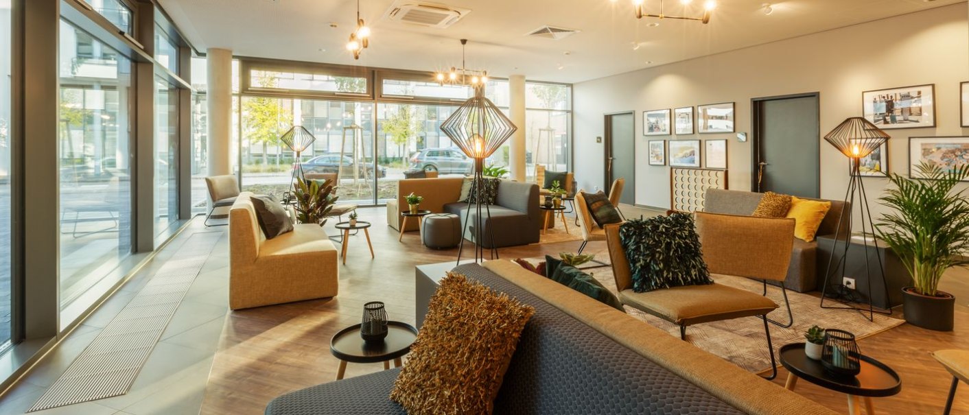 Moderne Lobby mit gemütlichen Sitzgelegenheiten, Pflanzen und großen Fenstern. Dezente Beleuchtung und Wanddekorationen schaffen eine einladende Atmosphäre., © Novum Hospitality Moderne Lobby mit gemütlichen Sitzgelegenheiten, Pflanzen und großen Fenstern. Dezente Beleuchtung und Wanddekorationen schaffen eine einladende Atmosphäre., © Novum Hospitality