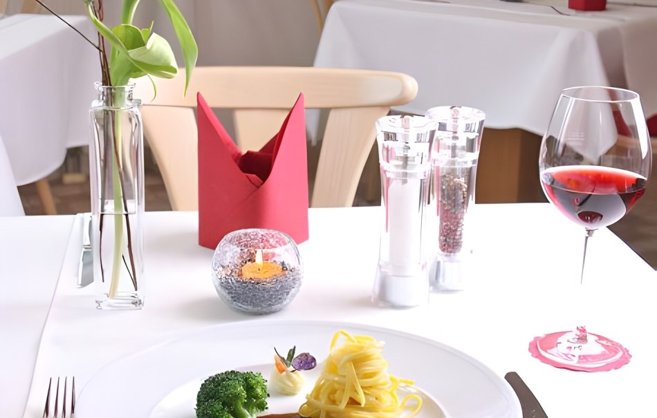 Ein elegant gedeckter Tisch in einem Restaurant mit Teller, Besteck, Weinglas, Kerze und Blume. Das Gericht besteht aus Fleisch, Nudeln und Brokkoli., © Hotel Neuwirtshaus