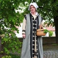 Eine Frau in historischer Kleidung h&auml;lt einen Korb und steht auf einem gepflasterten Weg unter einem Baum. Sie tr&auml;gt ein langes Gewand und eine wei&szlig;e Haube., &copy; Stadt Leonberg
