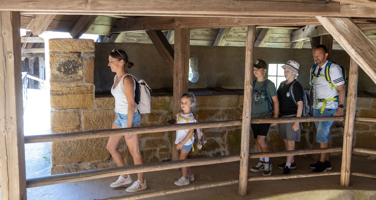 Eine Familie mit Rucks&auml;cken geht durch einen h&ouml;lzernen Gang in einer Burgruine. Die Sonne scheint durch das Dach., &copy; Foto Thomas Zehnder