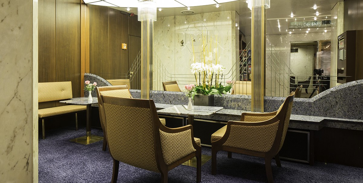 Elegante Sitzecke mit gepolsterten Sesseln, einem Tisch und Blumenarrangement. Holzvertäfelung und moderne Beleuchtung schaffen eine stilvolle Atmosphäre., © Hotel Royal Elegante Sitzecke mit gepolsterten Sesseln, einem Tisch und Blumenarrangement. Holzvertäfelung und moderne Beleuchtung schaffen eine stilvolle Atmosphäre., © Hotel Royal