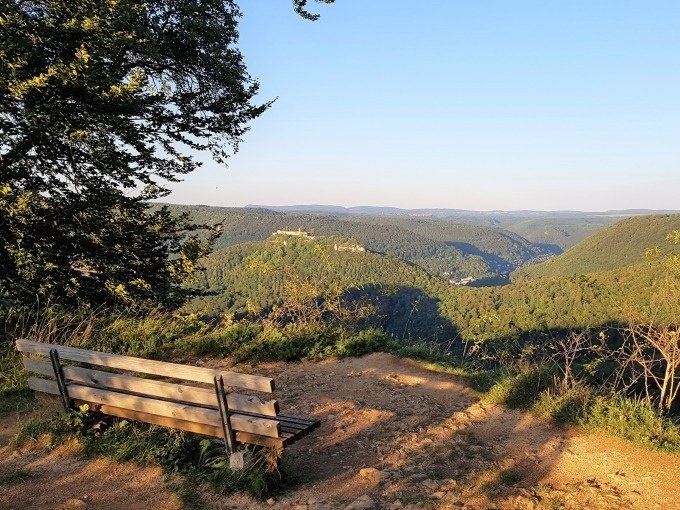 Holzbank auf einem H&uuml;gel mit Blick auf bewaldete T&auml;ler und H&uuml;gel unter klarem Himmel., &copy; SwabianTravel
