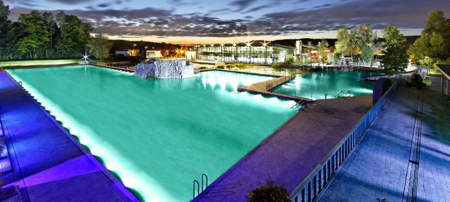 Beleuchtetes Freibad bei Nacht mit türkisfarbenem Wasser, umgeben von Bäumen und Gebäuden im Hintergrund., © Oskar Frech SeeBad Beleuchtetes Freibad bei Nacht mit türkisfarbenem Wasser, umgeben von Bäumen und Gebäuden im Hintergrund., © Oskar Frech SeeBad