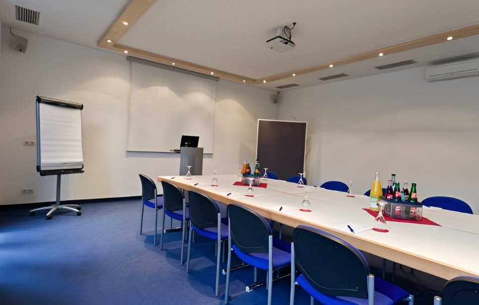 Moderner Konferenzraum mit großem Tisch, blauen Stühlen, Flipchart und Getränken. An der Decke ein Projektor, an der Wand eine Leinwand., © Hotel Neuwirtshaus Moderner Konferenzraum mit großem Tisch, blauen Stühlen, Flipchart und Getränken. An der Decke ein Projektor, an der Wand eine Leinwand., © Hotel Neuwirtshaus