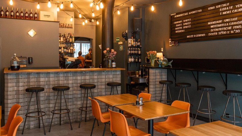 Gem&uuml;tliche Bar mit Holztischen, Barhockern und einer Theke. Lichterketten und ein Men&uuml;brett schm&uuml;cken die Wand., &copy; SMG, Sarah Schmid