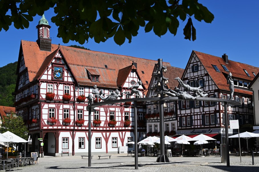 Fachwerkh&auml;user und eine Skulpturengruppe zieren den Marktplatz von Bad Urach. Die Geb&auml;ude sind mit roten Blumen geschm&uuml;ckt, der Himmel ist klar und blau., &copy; Bad Urach Tourismus