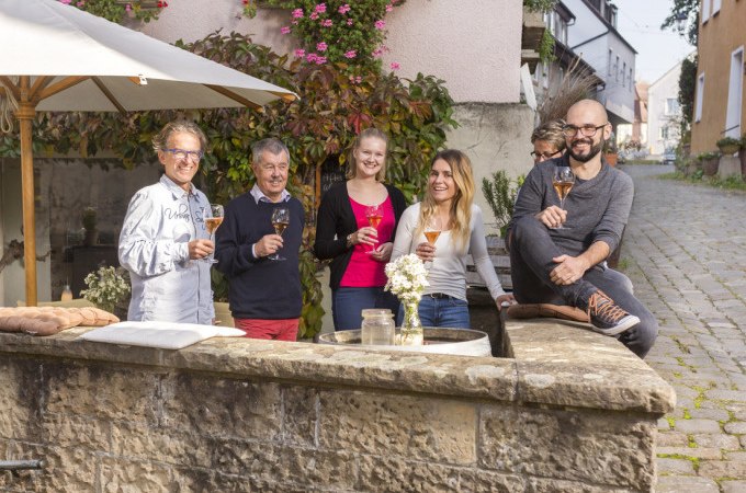 Eine fr&ouml;hliche Gruppe genie&szlig;t Wein an einem Brunnen in einer malerischen Gasse mit Blumen und Kopfsteinpflaster., &copy; Stadt N&uuml;rtingen