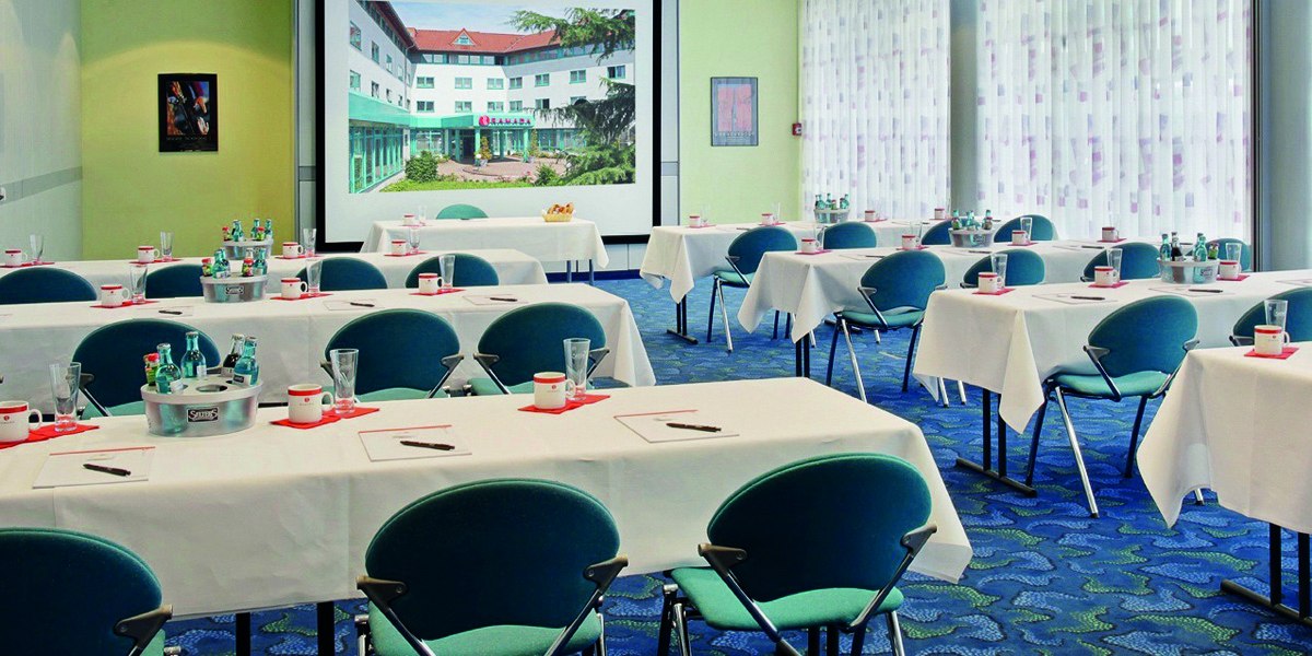 Ein Konferenzraum mit gedeckten Tischen, Stühlen und einer großen Leinwand. Wasserflaschen und Gläser stehen bereit., © © H-Hotels.com