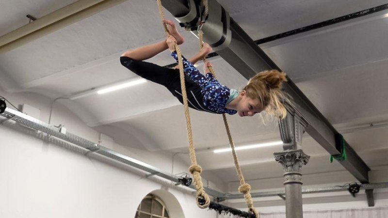 Ein M&auml;dchen in einem blauen Anzug macht Luftakrobatik an Seilen in einer Halle. Sie h&auml;ngt kopf&uuml;ber und h&auml;lt sich mit den F&uuml;&szlig;en fest., &copy; Kunstschule Labyrinth