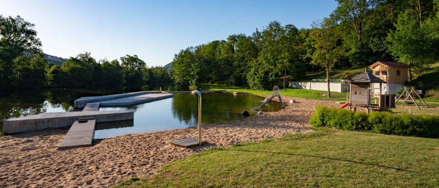 Das Kocherfreibad in K&uuml;nzelsau zeigt einen Sandstrand mit Rutsche, Spielplatz und umgebender Natur. Der Himmel ist klar und blau., &copy; Olivier Schniepp, Foto Linke GmbH