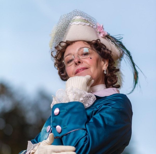 Eine Frau in historischer Kleidung mit einem verzierten Hut und Brille posiert selbstbewusst vor einem blauen Himmel., &copy; Quelle: Irma Beck