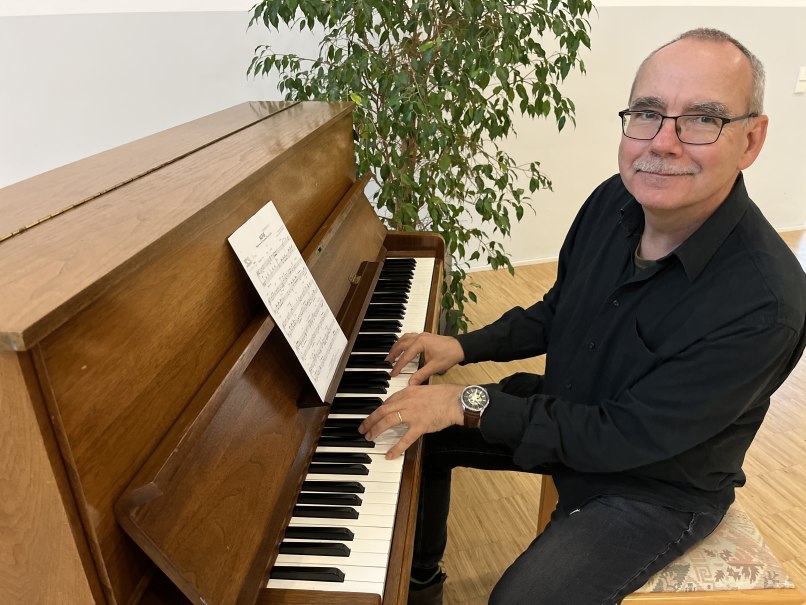 Ein Mann spielt an einem Holzklavier, l&auml;chelt und schaut in die Kamera. Im Hintergrund steht eine Pflanze., &copy; Klaus Leonhardt