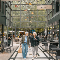 Zwei Personen spazieren durch die Calwer Passage mit Geschäften und Cafés. Die Passage hat ein Glasdach und ist modern gestaltet., © Stuttgart-Marketing GmbH, Sarah Schmid