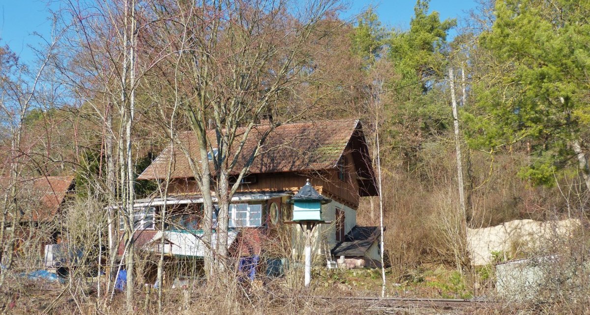 Ein ehemaliges Bahnwärterhaus steht inmitten von Bäumen und Sträuchern. Das Gebäude hat ein schräges Dach und ist von Natur umgeben., © Natur.Nah. Schönbuch & Heckengäu Ein ehemaliges Bahnwärterhaus steht inmitten von Bäumen und Sträuchern. Das Gebäude hat ein schräges Dach und ist von Natur umgeben., © Natur.Nah. Schönbuch & Heckengäu