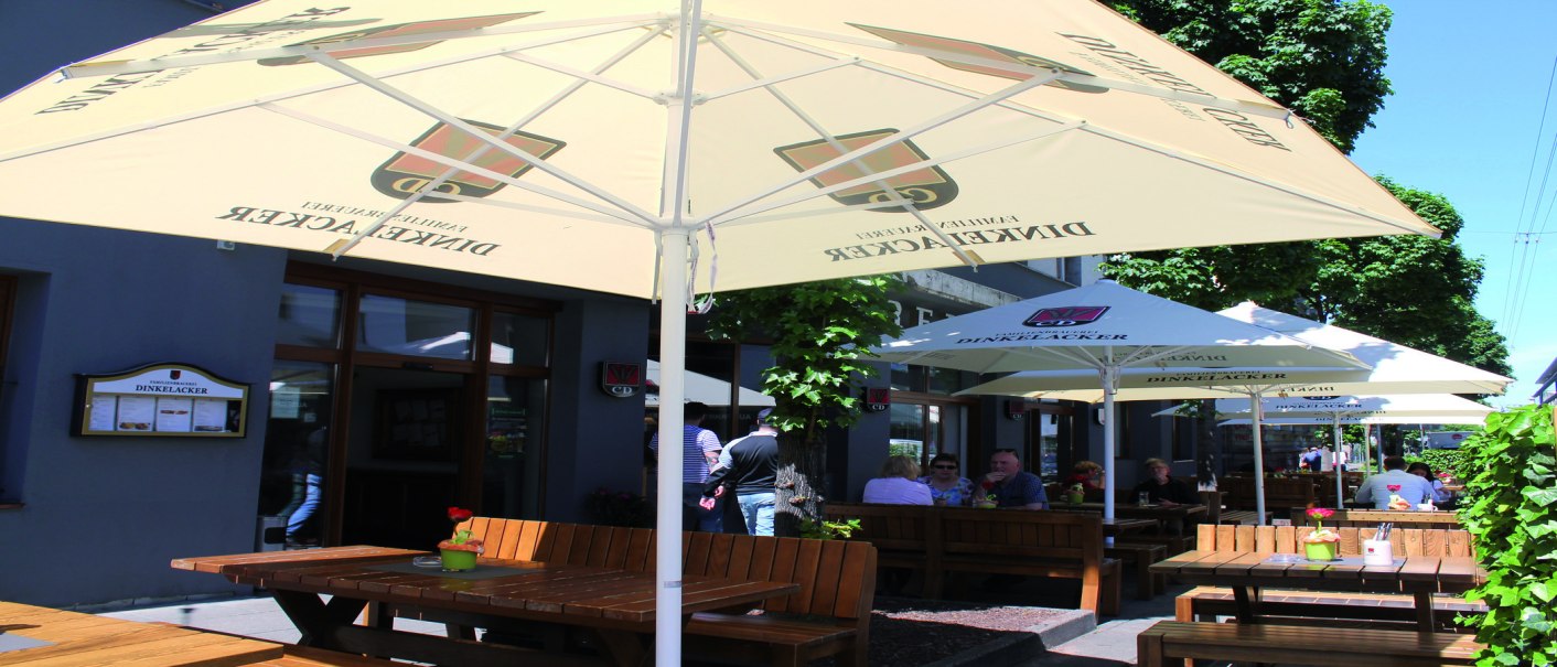 Außenbereich der Brauereigaststätte Dinkelacker mit Holzbänken und Sonnenschirmen. Gäste sitzen im Schatten und genießen das Wetter., © Stuttgart-Marketing GmbH