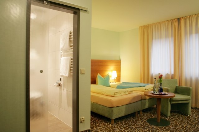 Gemütliches Doppelzimmer mit Bett, Tisch, Stühlen und angrenzendem Badezimmer. Helle Vorhänge und Teppichboden sorgen für eine einladende Atmosphäre., © ateckhotel Gemütliches Doppelzimmer mit Bett, Tisch, Stühlen und angrenzendem Badezimmer. Helle Vorhänge und Teppichboden sorgen für eine einladende Atmosphäre., © ateckhotel