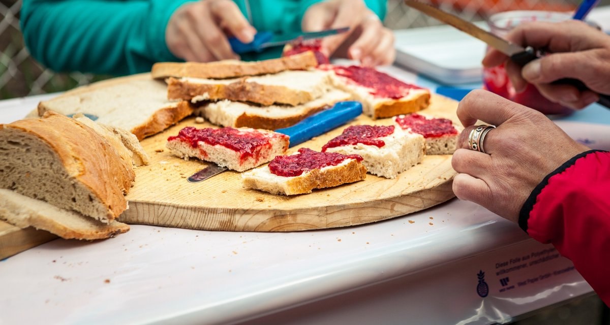 Zwei Personen schmieren Marmelade auf Brotscheiben auf einem Holzteller. Einfache Brotzeit im Freien., &copy; hochgehberge