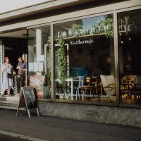 Menschen unterhalten sich vor dem LABYRINTH Kulturzentrum & -café. Die Fenster sind mit Pflanzen dekoriert, und ein Schild steht vor dem Eingang., © Christoph Steinweg
