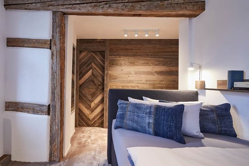 Schlafzimmer mit Holzbalken, modernem Bett, blauen Kissen und Holzverkleidung. Warmes Licht sorgt für eine gemütliche Atmosphäre., © Hotel Restaurant Bachofer Schlafzimmer mit Holzbalken, modernem Bett, blauen Kissen und Holzverkleidung. Warmes Licht sorgt für eine gemütliche Atmosphäre., © Hotel Restaurant Bachofer