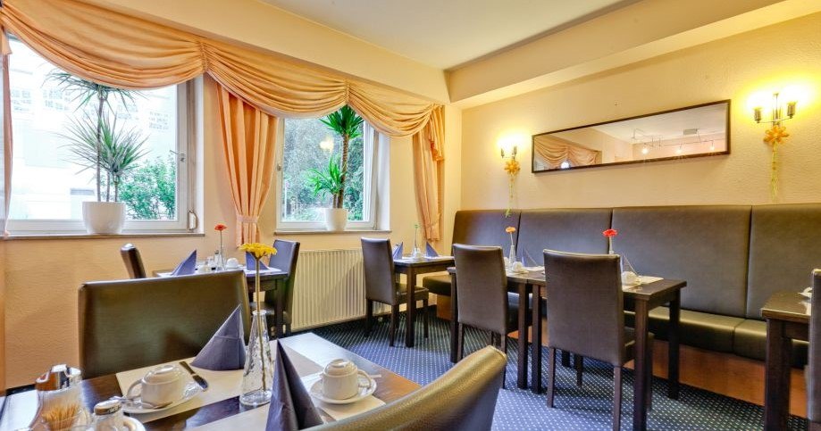Ein gemütlicher Frühstücksraum mit gedeckten Tischen, Pflanzen auf der Fensterbank und eleganten Vorhängen. Ein Spiegel hängt an der Wand., © ARNOTEL GmbH Ein gemütlicher Frühstücksraum mit gedeckten Tischen, Pflanzen auf der Fensterbank und eleganten Vorhängen. Ein Spiegel hängt an der Wand., © ARNOTEL GmbH