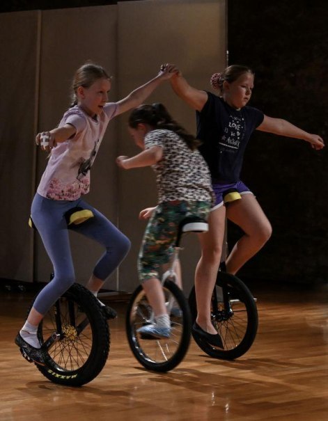 Drei Kinder fahren auf Einrädern in einer Halle. Zwei halten sich an den Händen, während das dritte Kind in der Mitte fährt., © Kunstschule Labyrinth Drei Kinder fahren auf Einrädern in einer Halle. Zwei halten sich an den Händen, während das dritte Kind in der Mitte fährt., © Kunstschule Labyrinth